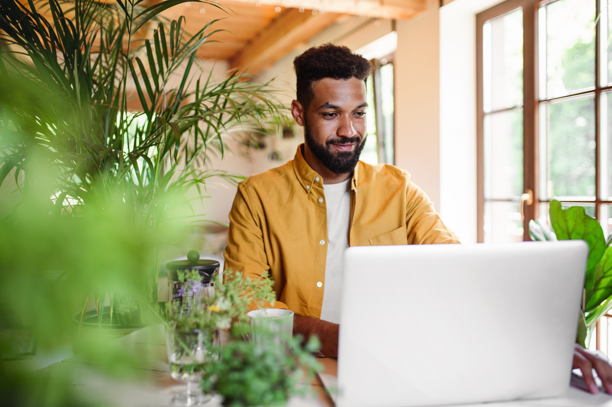 A young man with laptop and coffee working indoors on Rainbow