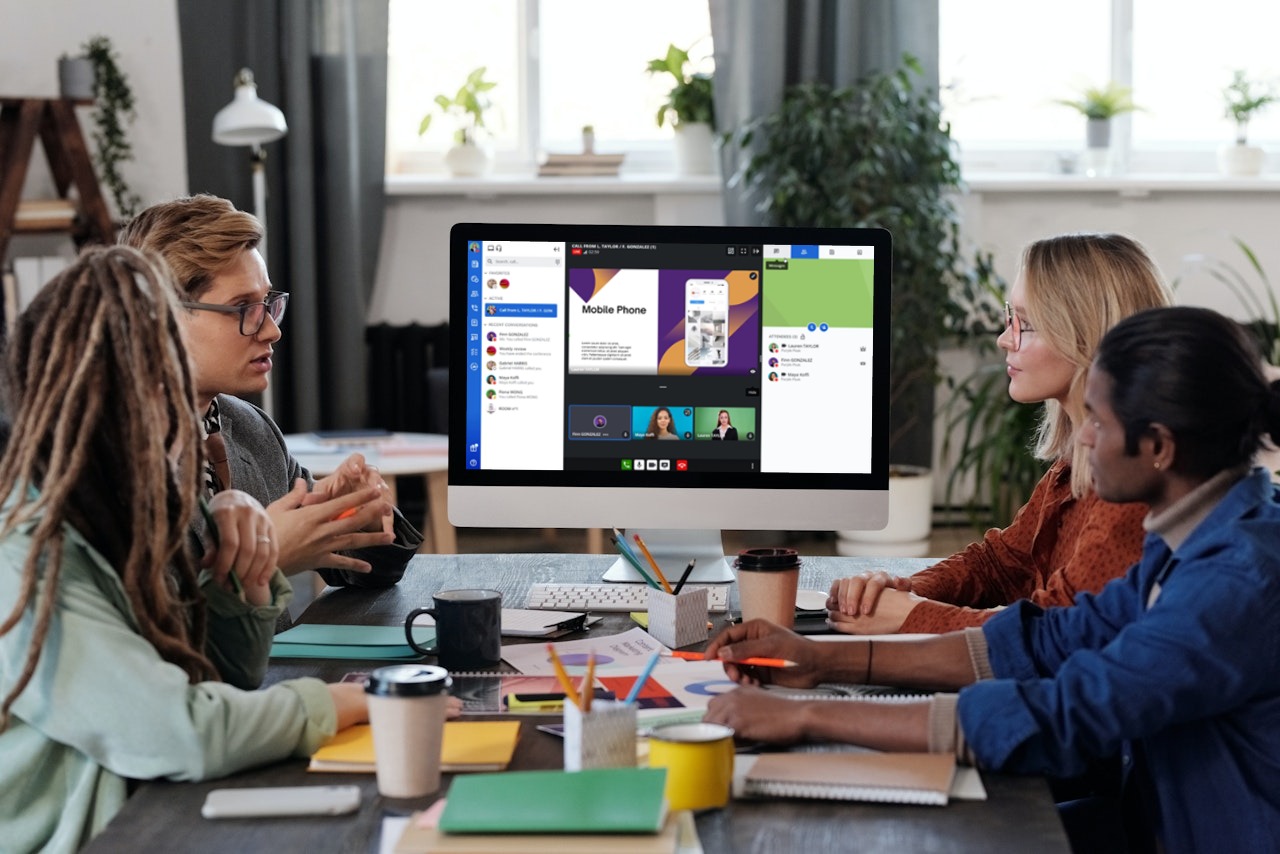 Group of professionals having a meeting and looking towards a desktop showing Rainbow on the screen